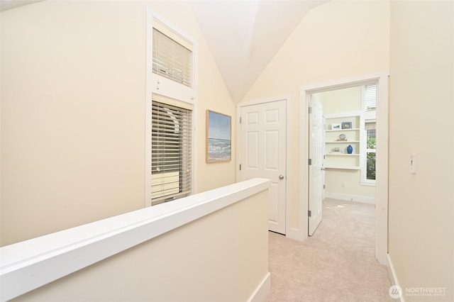 hallway featuring baseboards, light carpet, and lofted ceiling