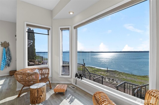 sunroom / solarium with visible vents, wood finished floors, baseboards, and a water view