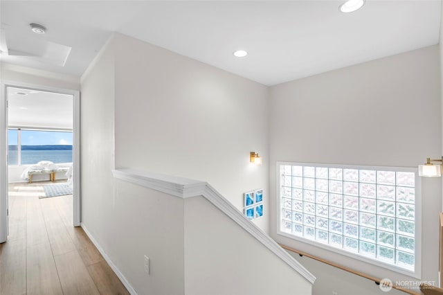hall featuring recessed lighting, a water view, an upstairs landing, baseboards, and light wood-style flooring