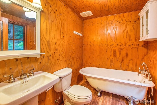 bathroom featuring a sink, a freestanding bath, toilet, and wooden walls