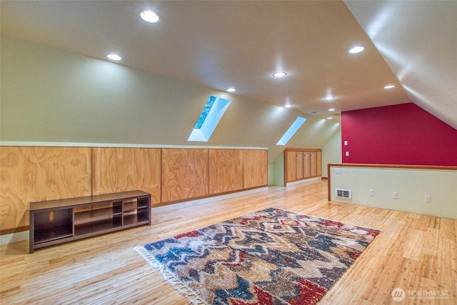 additional living space featuring visible vents, light wood-type flooring, and vaulted ceiling with skylight