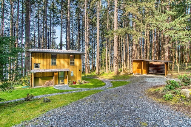 view of front of home with a wooded view, an outbuilding, metal roof, gravel driveway, and a standing seam roof