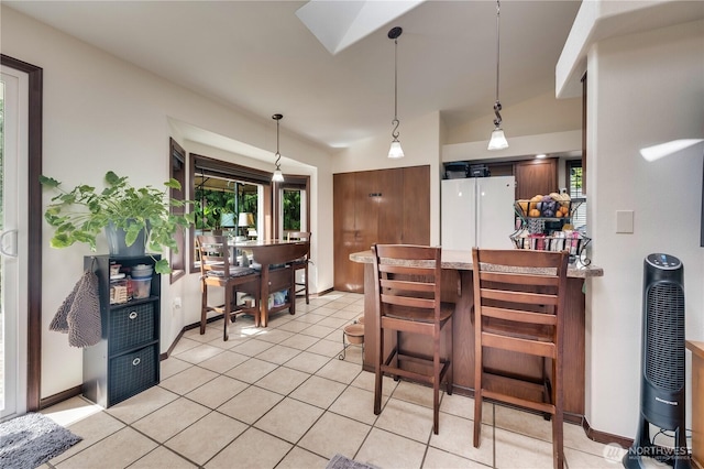 kitchen with a breakfast bar, a peninsula, freestanding refrigerator, light tile patterned flooring, and hanging light fixtures