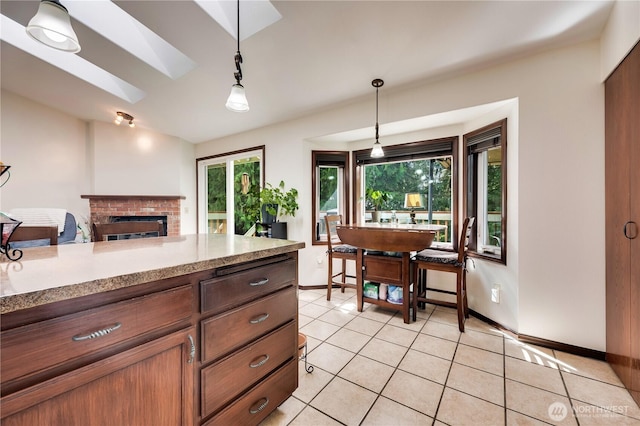 kitchen featuring vaulted ceiling with skylight, decorative light fixtures, light countertops, a fireplace, and light tile patterned flooring