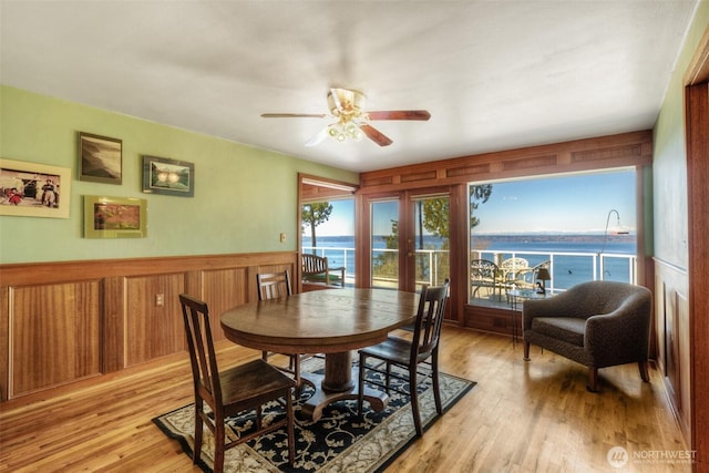 dining space with a ceiling fan, wainscoting, light wood-style flooring, and a water view