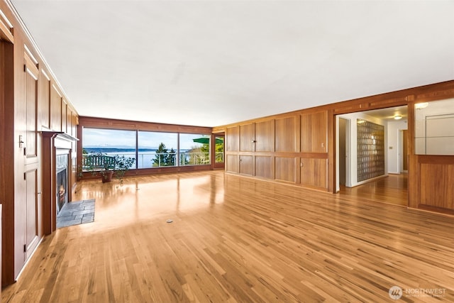 unfurnished living room featuring wood walls, a fireplace with raised hearth, and light wood-type flooring