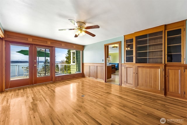 unfurnished room with french doors, light wood finished floors, ceiling fan, and wainscoting