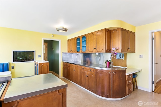 kitchen with brown cabinets, baseboards, decorative backsplash, and stainless steel countertops