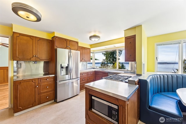 kitchen featuring brown cabinetry, a peninsula, appliances with stainless steel finishes, and stainless steel counters