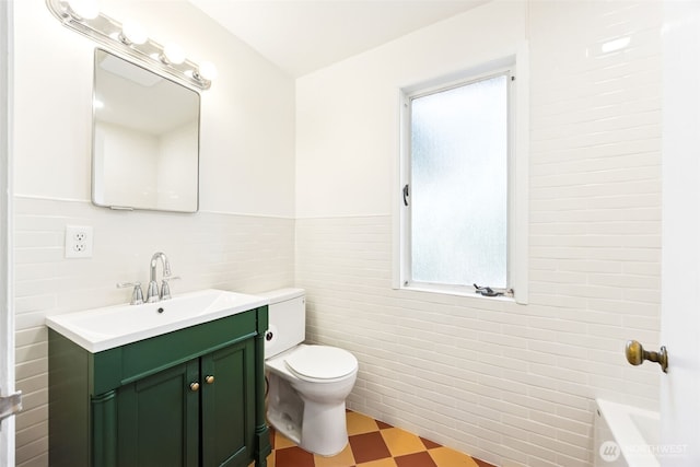 full bath featuring vanity, wainscoting, toilet, tile walls, and tile patterned floors