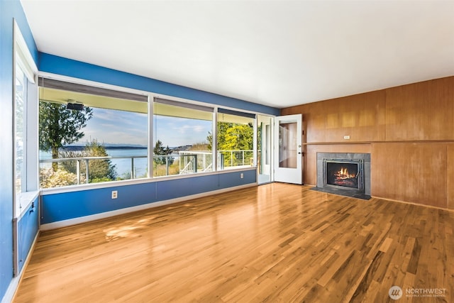 unfurnished living room featuring baseboards, a premium fireplace, wood finished floors, and a wealth of natural light