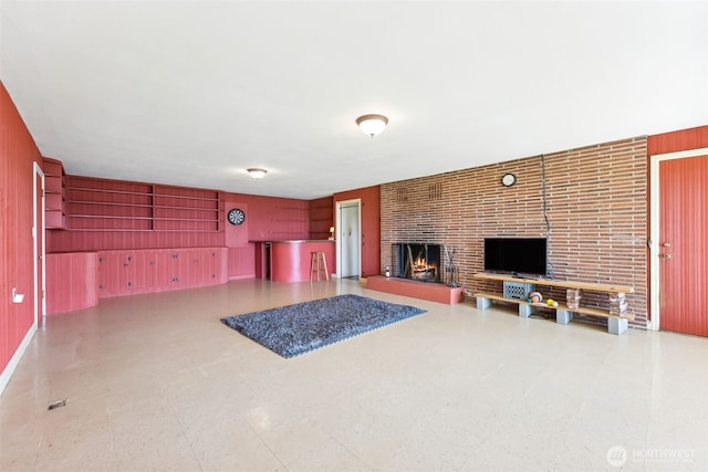 unfurnished living room featuring a brick fireplace, tile patterned floors, and wood walls