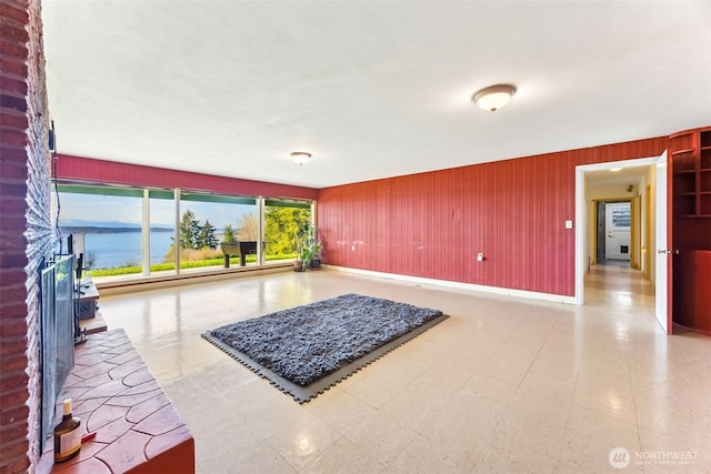 living area with wooden walls, a water view, and baseboards