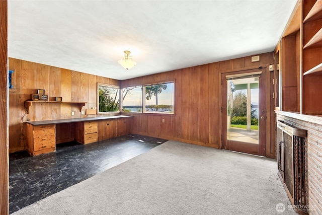 unfurnished office with dark carpet, wood walls, and built in desk