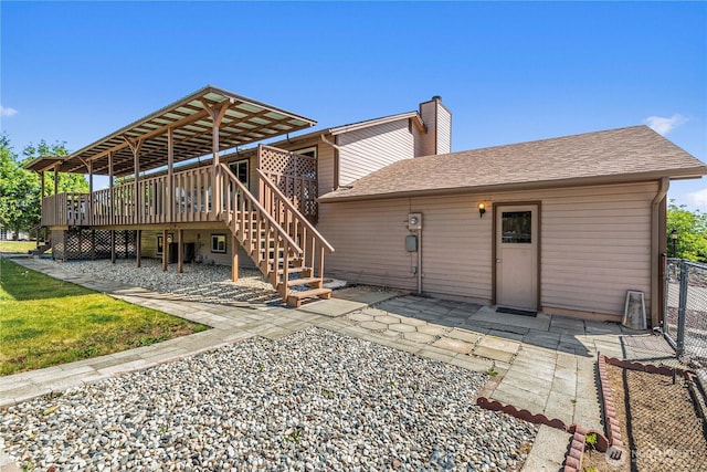 rear view of house featuring a deck, stairway, a chimney, roof with shingles, and a patio area