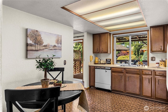 kitchen featuring white dishwasher, a sink, light countertops, a textured ceiling, and a textured wall
