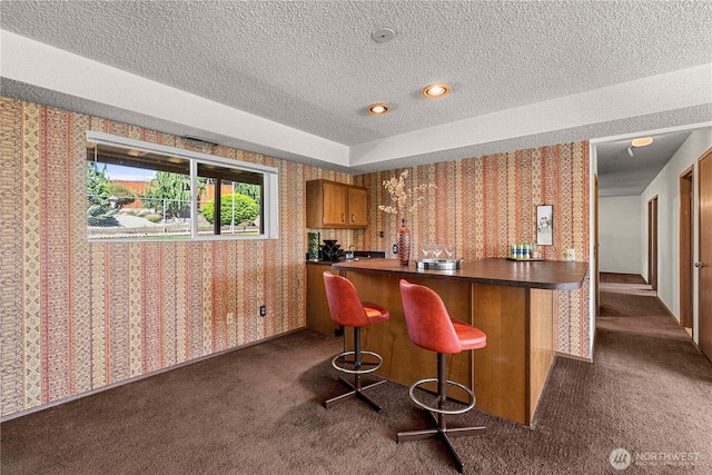 bar area with wallpapered walls, a textured ceiling, and dark colored carpet