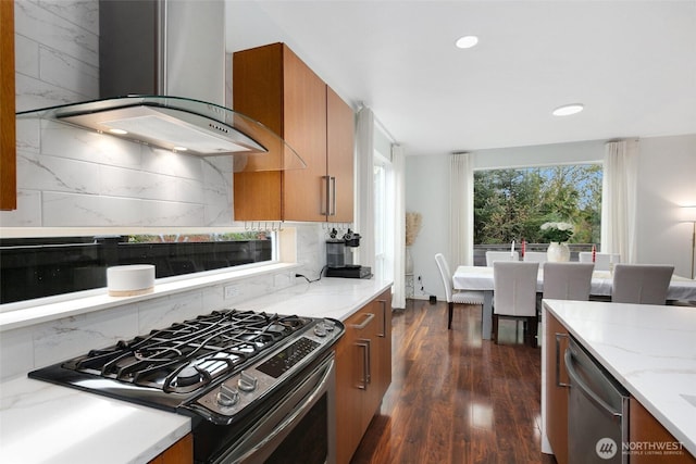 kitchen featuring wall chimney range hood, brown cabinets, dark wood-style floors, light stone countertops, and appliances with stainless steel finishes