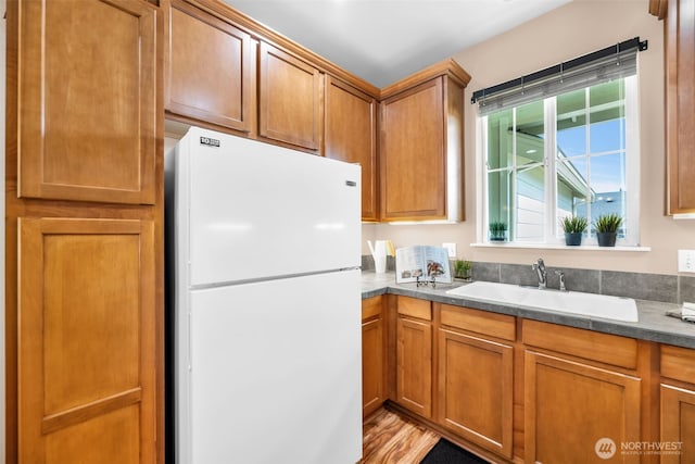 kitchen with freestanding refrigerator, brown cabinets, a sink, and light wood finished floors