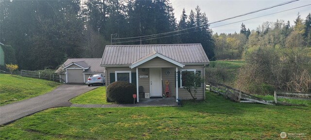 bungalow-style home featuring a wooded view, a front yard, metal roof, and fence