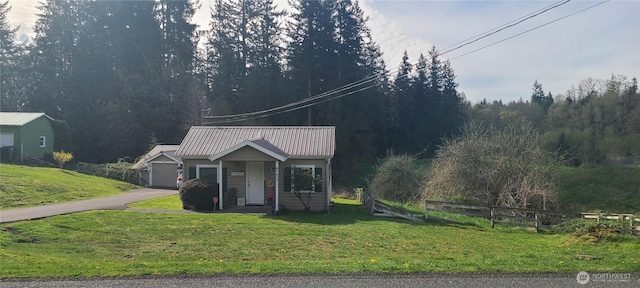 view of front of home featuring a wooded view, metal roof, fence, a front lawn, and driveway