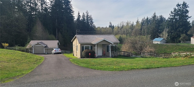 view of front of property with aphalt driveway, a front yard, a forest view, metal roof, and fence