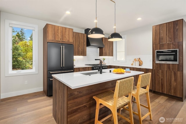 kitchen with tasteful backsplash, light wood-type flooring, light countertops, appliances with stainless steel finishes, and a sink