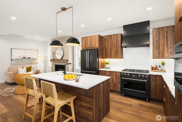 kitchen featuring wall chimney range hood, black appliances, a kitchen breakfast bar, and wood finished floors