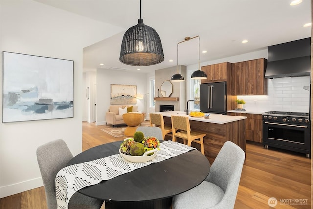 dining room featuring recessed lighting, a fireplace, light wood-style flooring, and baseboards