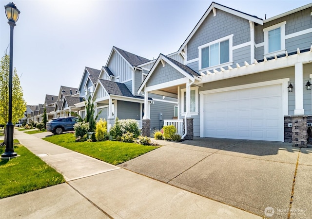 craftsman house featuring concrete driveway, a residential view, stone siding, an attached garage, and a front lawn
