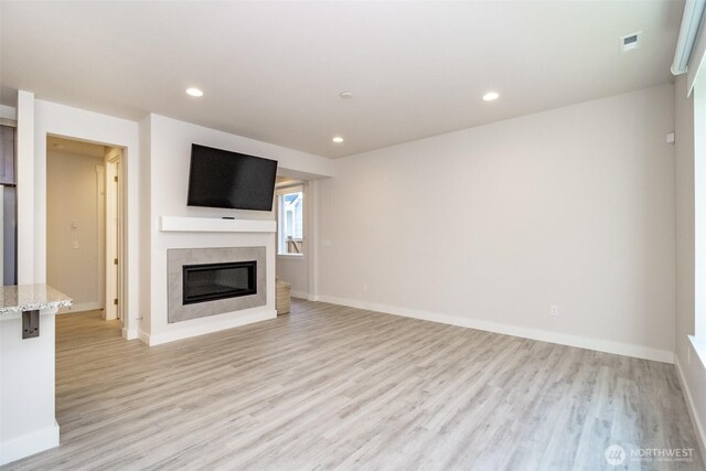 unfurnished living room with a glass covered fireplace, recessed lighting, baseboards, and light wood-type flooring