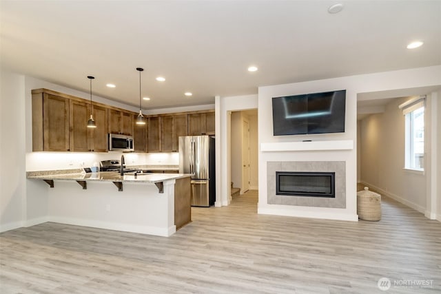 kitchen with stainless steel appliances, a kitchen breakfast bar, light wood-style flooring, a peninsula, and open floor plan