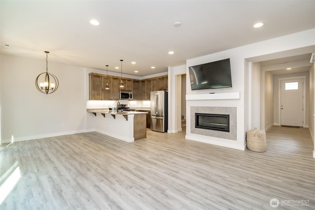 kitchen featuring a peninsula, stainless steel appliances, light countertops, open floor plan, and a kitchen breakfast bar