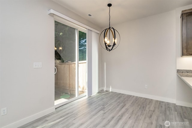 unfurnished dining area featuring wood finished floors, a notable chandelier, and baseboards