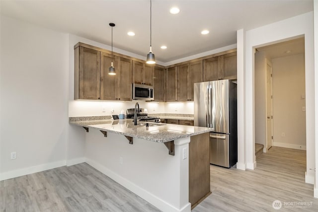 kitchen featuring light wood-style flooring, light stone counters, a breakfast bar area, stainless steel appliances, and a peninsula