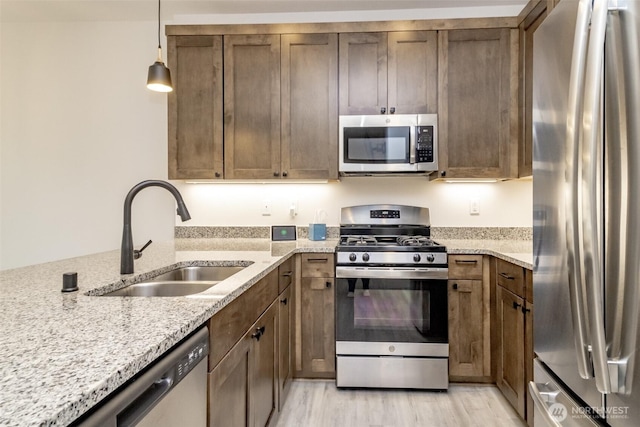 kitchen featuring light stone countertops, stainless steel appliances, light wood-style floors, a sink, and pendant lighting