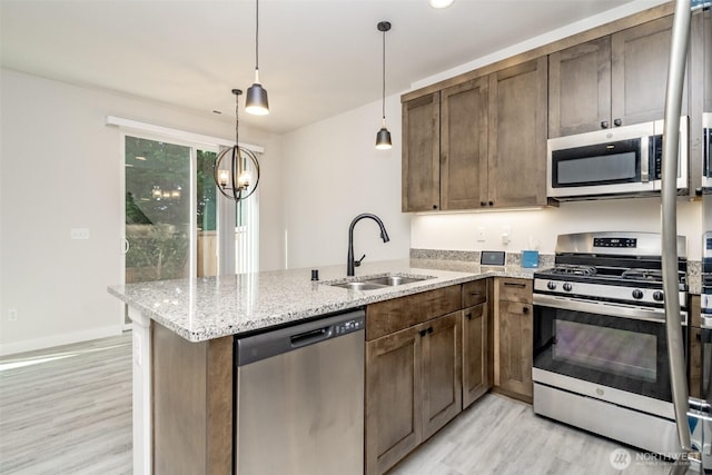 kitchen featuring stainless steel appliances, light wood-style floors, a peninsula, and a sink