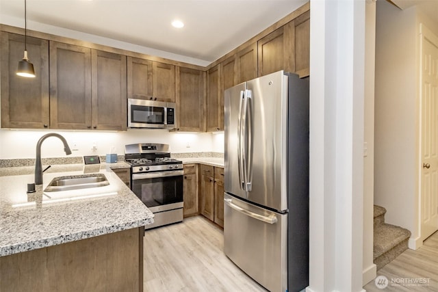 kitchen with light stone countertops, hanging light fixtures, light wood-style flooring, stainless steel appliances, and a sink