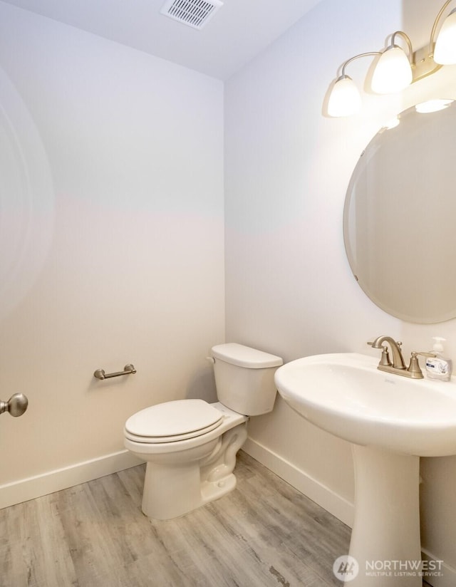 half bath with a sink, toilet, visible vents, baseboards, and wood finished floors