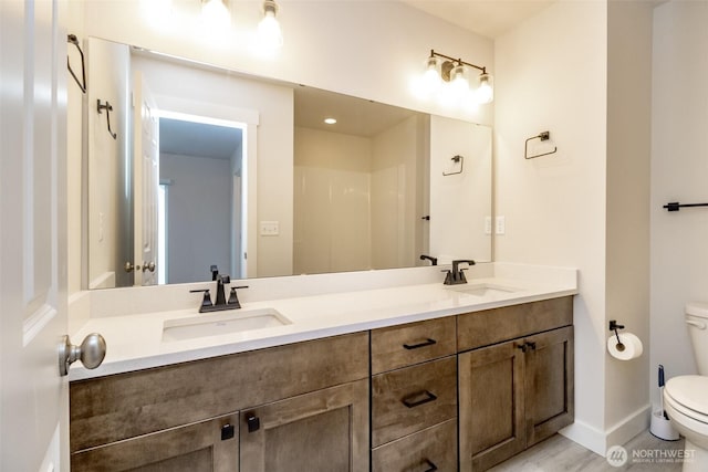 full bath featuring baseboards, toilet, double vanity, and a sink