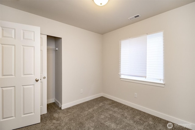 unfurnished bedroom with a closet, visible vents, dark colored carpet, and baseboards