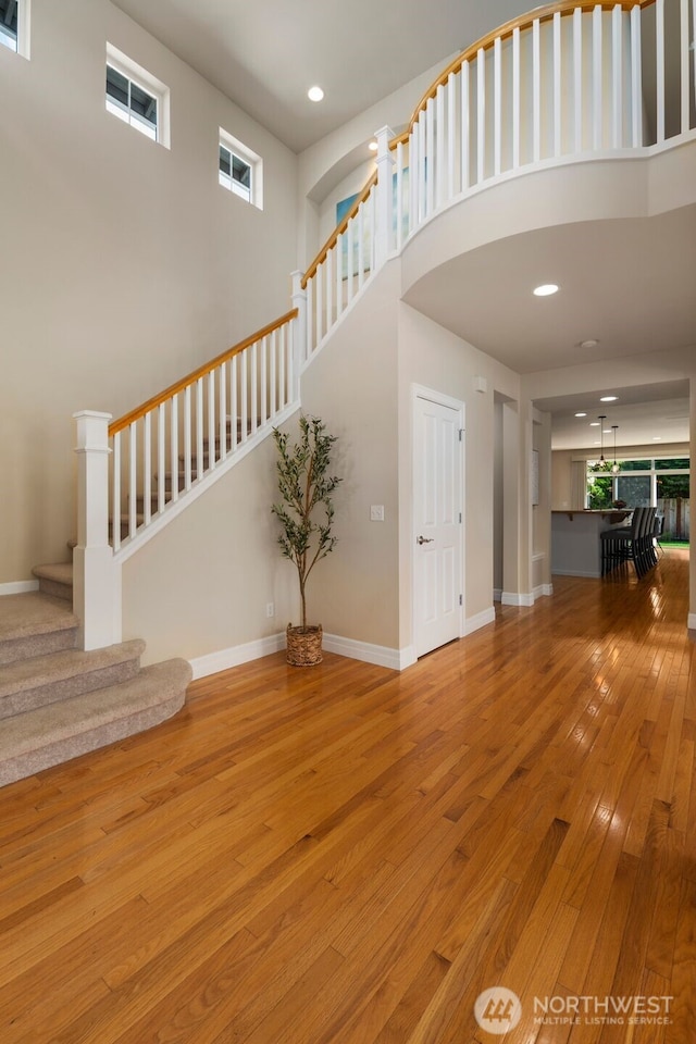 unfurnished living room featuring a high ceiling, baseboards, hardwood / wood-style flooring, and stairway