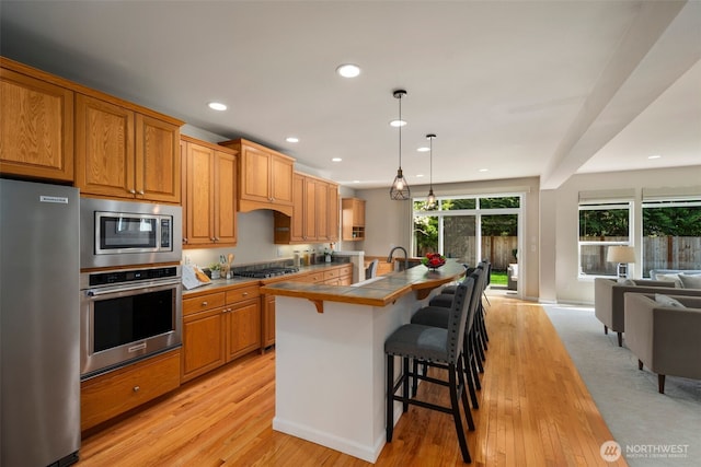 kitchen with tile countertops, a kitchen breakfast bar, light wood-style flooring, recessed lighting, and stainless steel appliances
