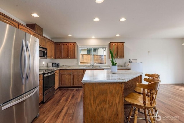 kitchen featuring dark wood-style flooring, a kitchen island, a kitchen breakfast bar, light stone counters, and appliances with stainless steel finishes