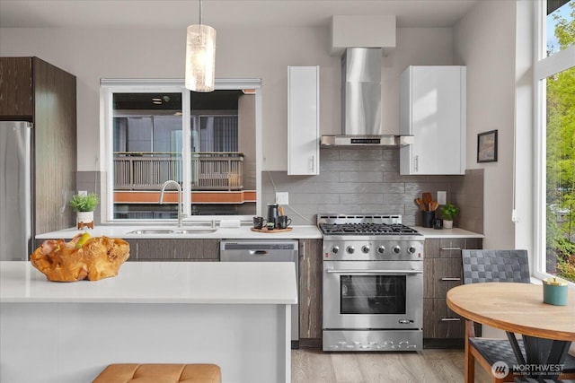 kitchen with tasteful backsplash, wall chimney exhaust hood, a sink, light countertops, and stainless steel appliances