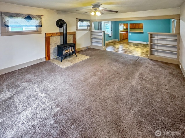 unfurnished living room featuring baseboards, stairway, a wood stove, ceiling fan, and carpet