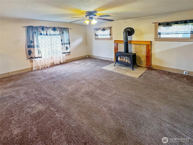 unfurnished living room with a wood stove, carpet, baseboards, and ceiling fan