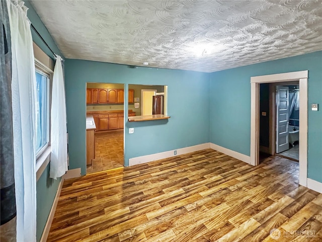 spare room with a textured ceiling, wood finished floors, and baseboards