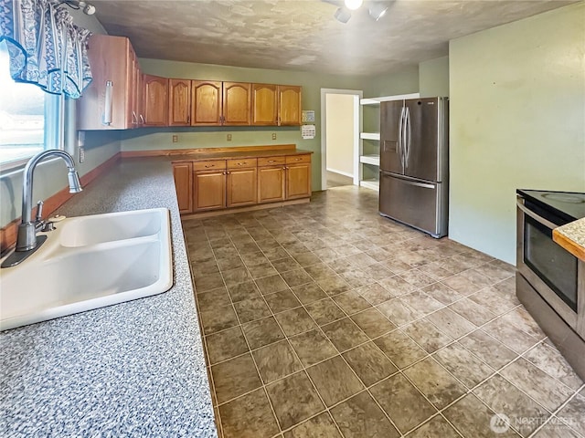kitchen featuring brown cabinetry, a textured ceiling, dark tile patterned flooring, appliances with stainless steel finishes, and a sink