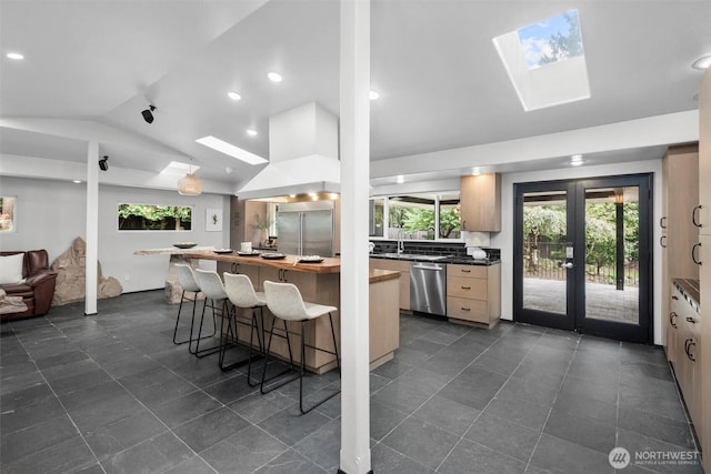 kitchen featuring vaulted ceiling with skylight, wall chimney range hood, a breakfast bar, appliances with stainless steel finishes, and plenty of natural light